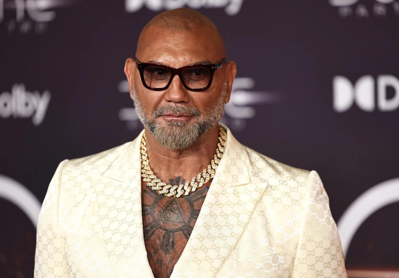 Dave Bautista w lutym 2024 roku Dave Bautista w jasnym garniturze i czarnych okularach, z brodą i tatuażami, na tle ścianki z logo