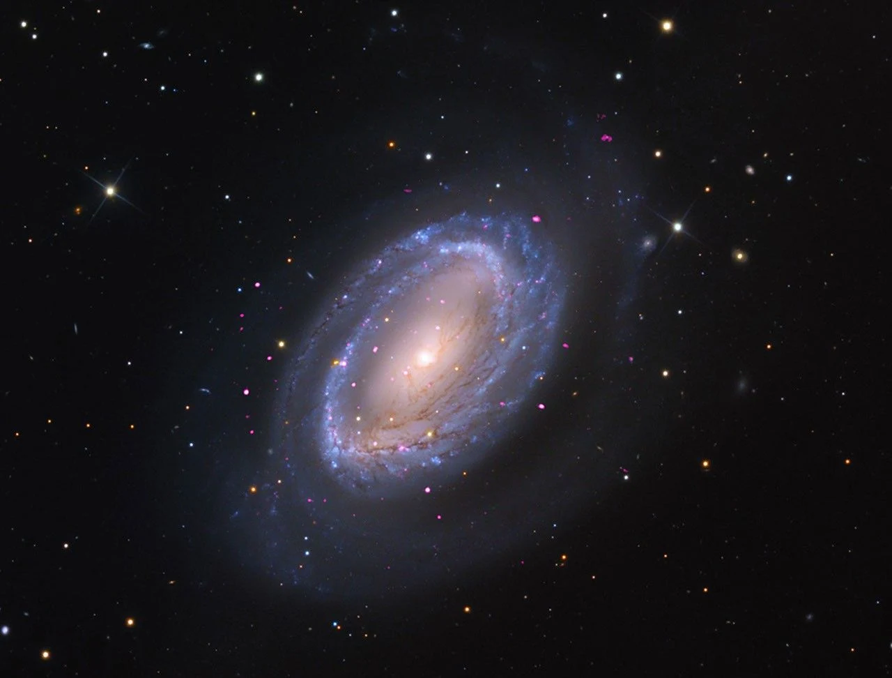 Spiralna galaktyka z wyraźnie zaznaczonymi ramionami i jasnym jądrem, otoczona licznymi gwiazdami na ciemnym tle kosmosu.