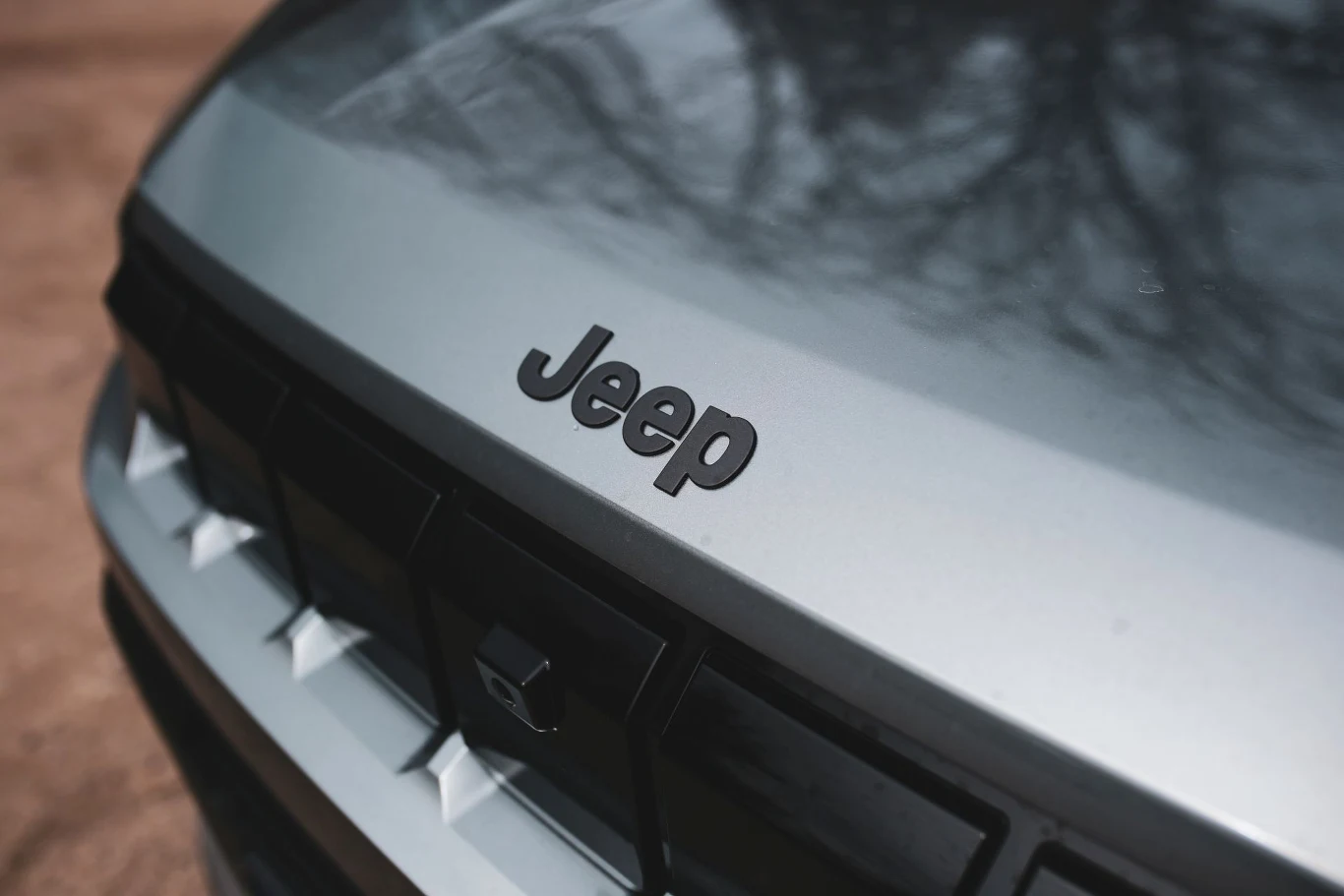 Siedmioszczelinowa osłona opcjonalnie może być podświetlana. Maska srebrnego samochodu marki Jeep z wyraźnie widocznym logo oraz fragmentem charakterystycznego grilla.