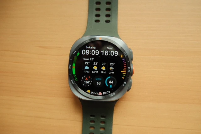 Smartwatch z zielonym silikonowym paskiem wyświetlający kolorowy ekran główny z aktualną godziną, prognozą pogody oraz różnymi wskaźnikami i powiadomieniami.