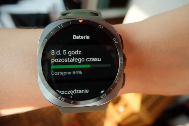 Smartwatch na nadgarstku wyświetlający informacje o stanie baterii, pokazuje 64% dostępnej energii oraz szacowany czas pracy na 3 dni i 5 godzin.