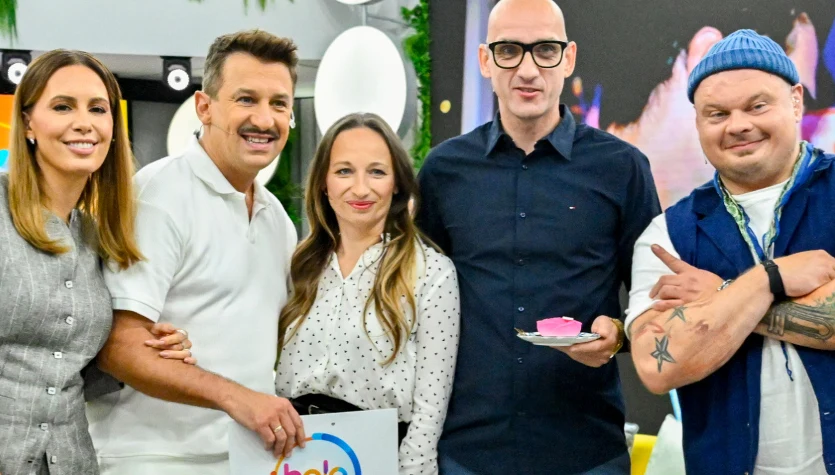 Pięć uśmiechniętych osób w kolorowych ubraniach pozuje razem w pomieszczeniu; jedna trzyma podkładkę z logo '"halo tu polsat", inna kawałek ciasta na talerzyku.