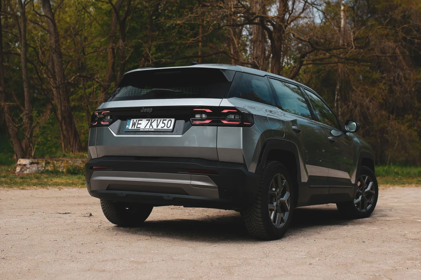 Prześwit Jeepa Compassa wynosi 20 cm, zaś głębokość brodzenia 47 cm. Srebrny SUV marki Jeep zaparkowany na nieutwardzonej nawierzchni, otoczony drzewami i roślinnością.