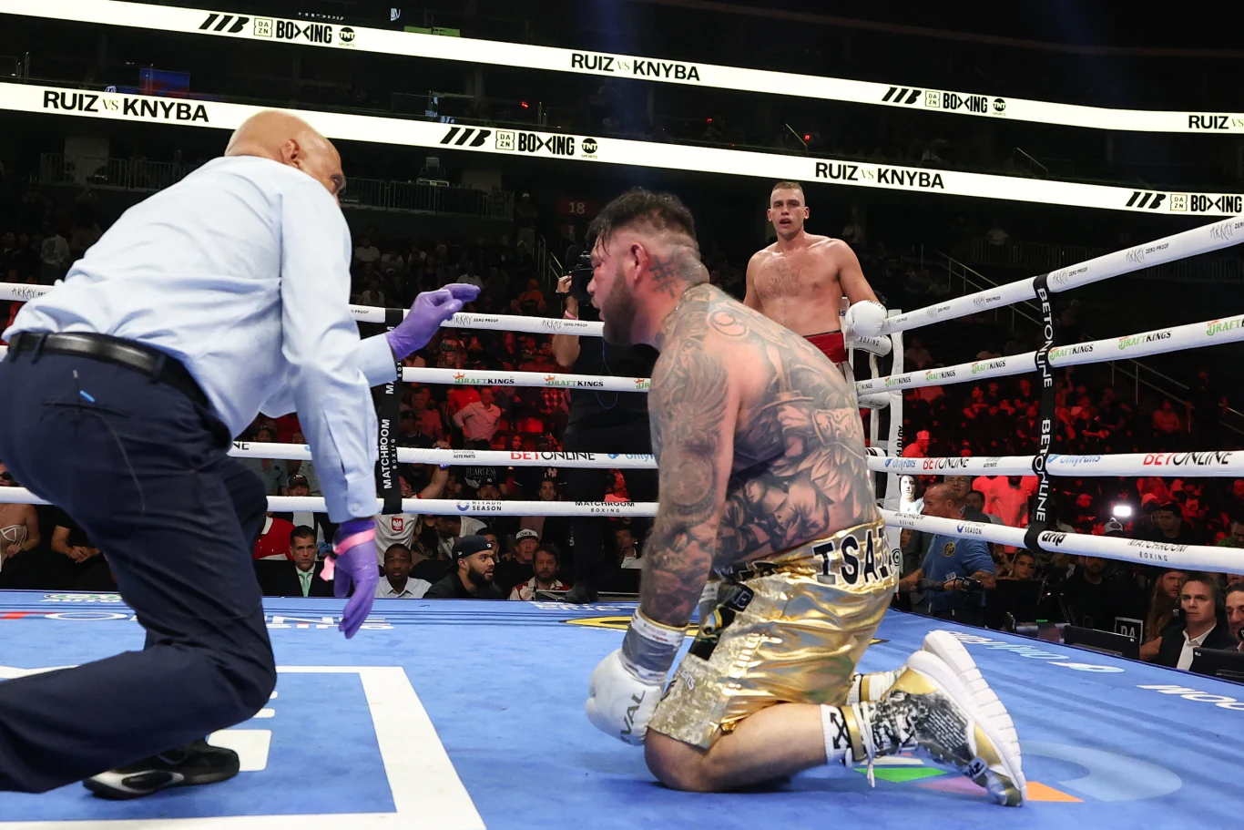 Andy Ruiz "podłączony do tlenu" przez sędziego ringowego. Damian Knyba został ograbiony ze zwycięstwa przed czasem Sędzia liczy zawodnika w złotych spodenkach klęczącego na ringu, podczas gdy drugi bokser w czerwonych rękawicach stoi w tle przy linach.