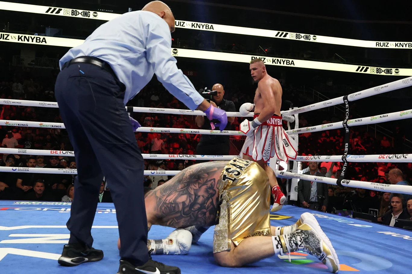 Andy Ruiz jr na deskach, Damian Knyba bezlitosny w Prudential Center Sędzia pochyla się nad zawodnikiem w złotych spodenkach klęczącym na ringu, podczas gdy drugi bokser w biało-czerwonych spodenkach stoi w narożniku, obserwując sytuację.