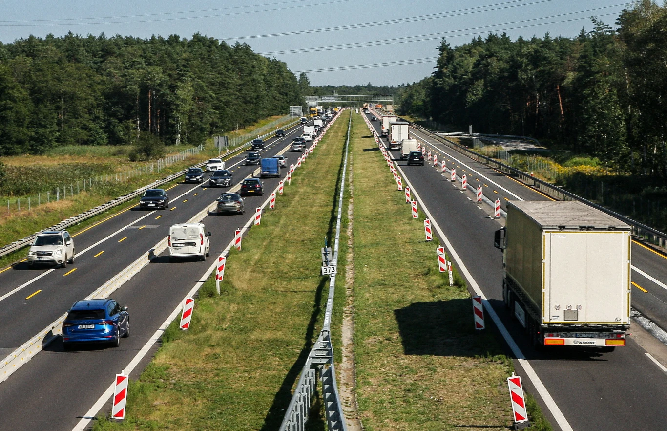 Autostrada A4 kojarzyła się kierowcom z wysokimi opłatami, kolejkami na bramkach i wiecznymi remontami. To wszystko wkrótce się zmieni Autostrada A4 z samochodami osobowymi i ciężarówkami, pas zieleni, barierki, znaki robót drogowych, las po bokach.