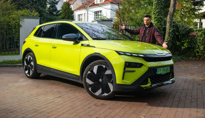 Jaskrawożółty samochód elektryczny marki Skoda w nowoczesnym, dynamicznym stylu zaparkowany na podjeździe, obok stoi mężczyzna w ciemnej kurtce z szeroko rozłożonymi rękami.