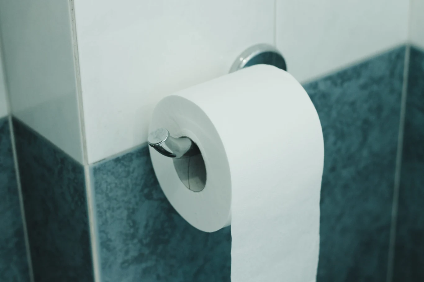 Jak poprawnie wieszać papier toaletowy - do przodu, czy do tyłu? Biała rolka papieru toaletowego na metalowym uchwycie przy ścianie.
