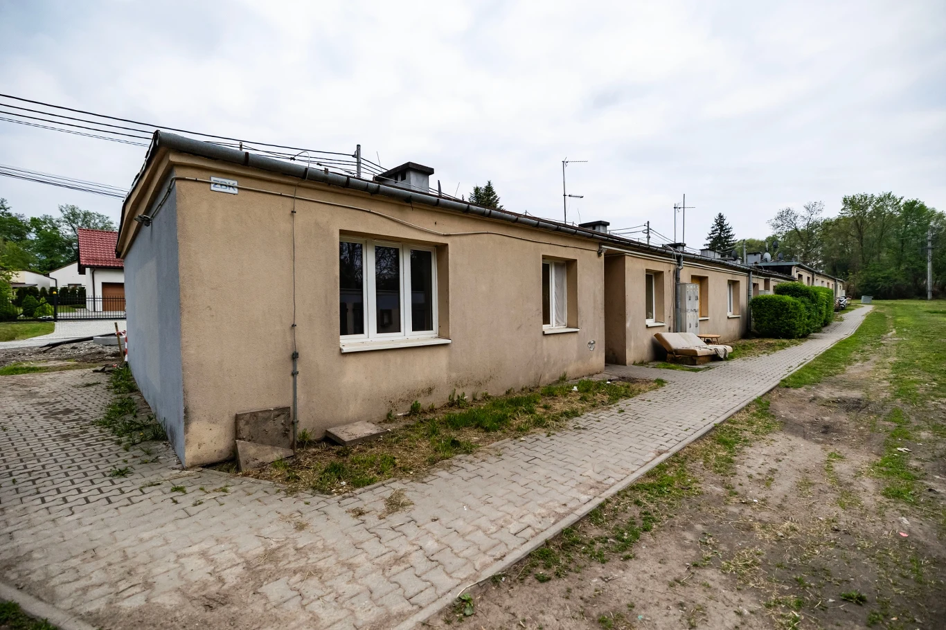 Osiedla powstają w miejscach, gdzie dostęp jest utrudniony Szereg niskich, jednokondygnacyjnych budynków mieszkalnych o szarej elewacji, z prostokątnymi oknami i drzwiami oraz utwardzoną ścieżką prowadzącą wzdłuż zabudowań.