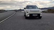 Nowoczesny, biały samochód SUV zaparkowany na szerokiej, asfaltowej drodze w otoczeniu górskiego krajobrazu i rozległego nieba z widocznymi chmurami.