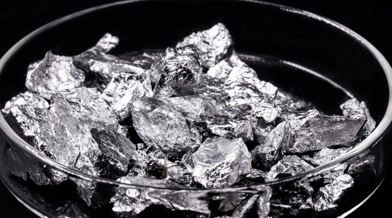 Amerykanie budują zakład do wydobywania metali ziem rzadkich z recyklingu. Bryły srebrzystego metalu w przezroczystym naczyniu laboratoryjnym, ilustracja recyklingu metali ziem rzadkich.