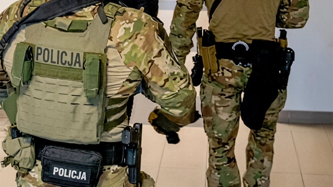 Zlecenie zabójstwa kilku osób udaremnione przez CBŚP Dwóch funkcjonariuszy CBŚP w taktycznych mundurach z napisem 'Policja' idzie korytarzem w budynku.