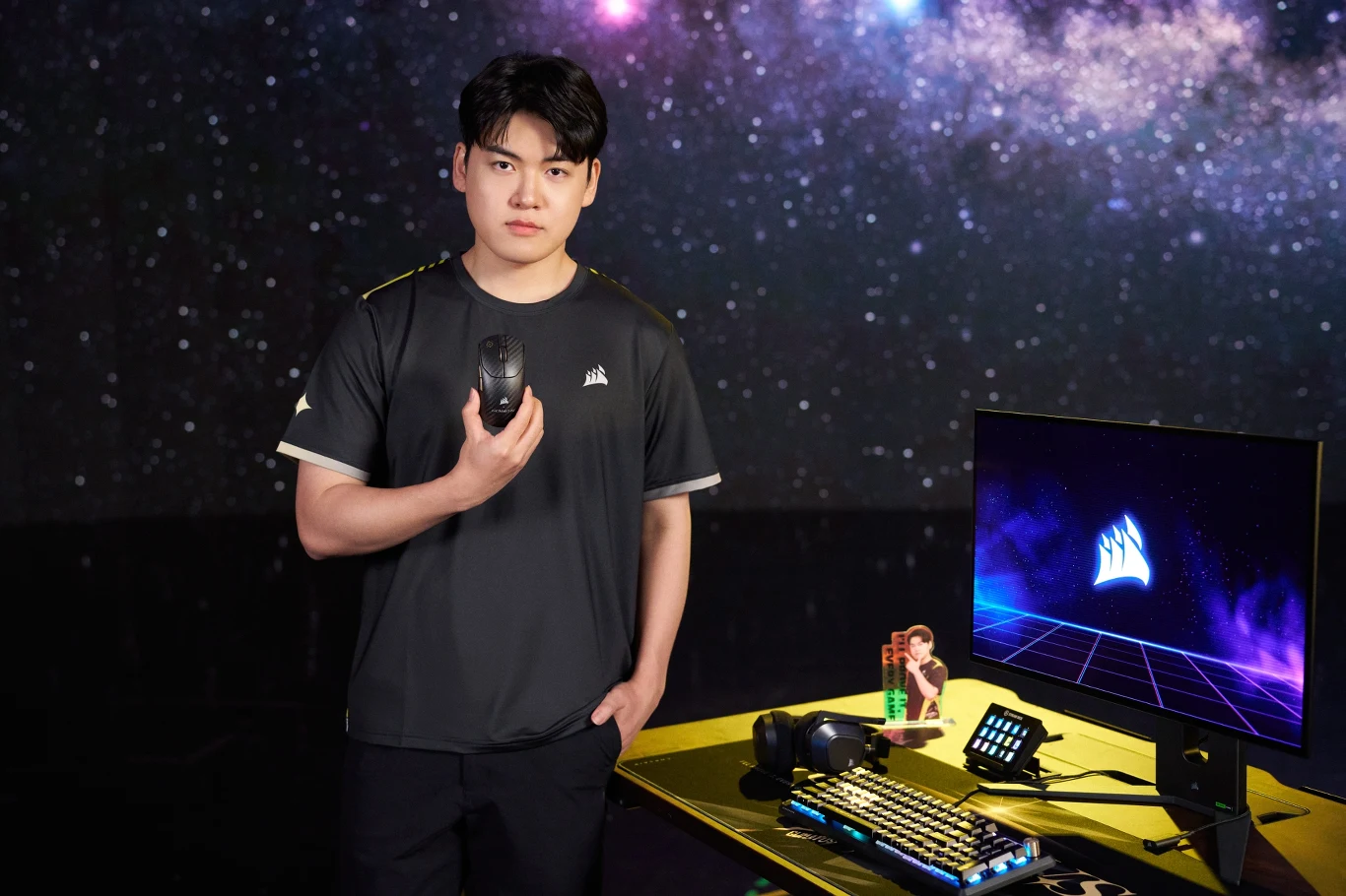 Corsair x Gumayusi Gumayusi przy stanowisku gamingowym Corsair z podświetlaną klawiaturą, myszką i monitorem z logo Corsair.
