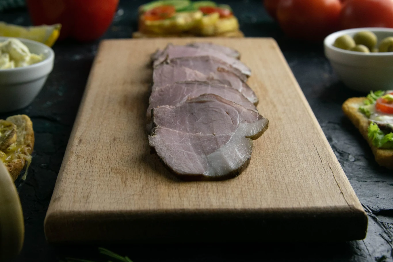 Wkładam mięso do lodówki na kilka dni. Potem mam najlepszą wędlinę na kanapki Domowa wędlina z karkówki pokrojona w cienkie plastry, podana na desce z pieczywem i dodatkami.