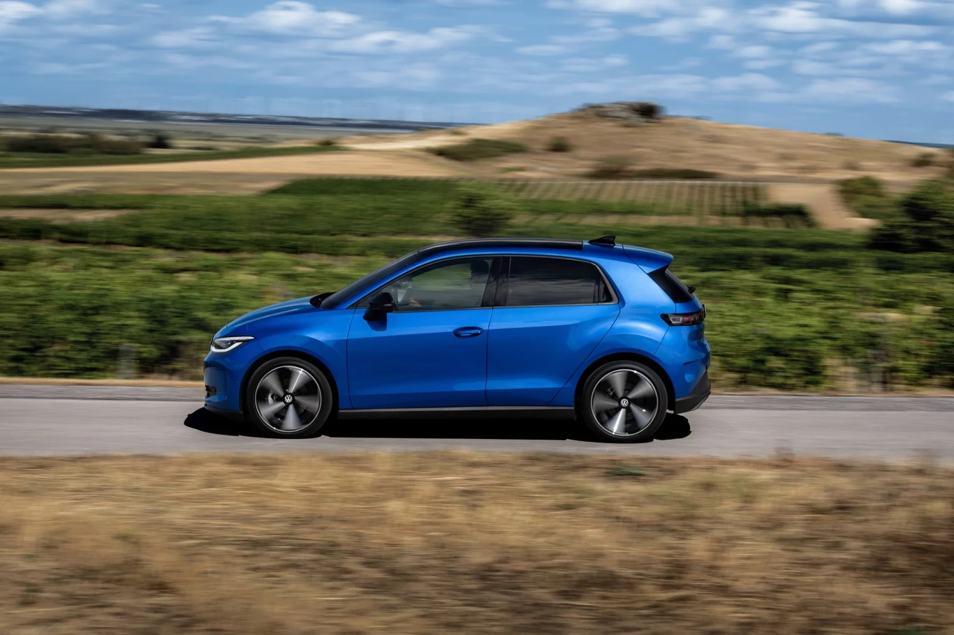 Volkswagen ID. Polo zapewnia na drodze przede wszystkim spokój - jest zwinny, przyczepny i przewidywalny, a do tego zaskakująco wręcz komfortowy. Niebieski samochód osobowy jedzie po wiejskiej drodze wśród zielonych pól i wzgórz.