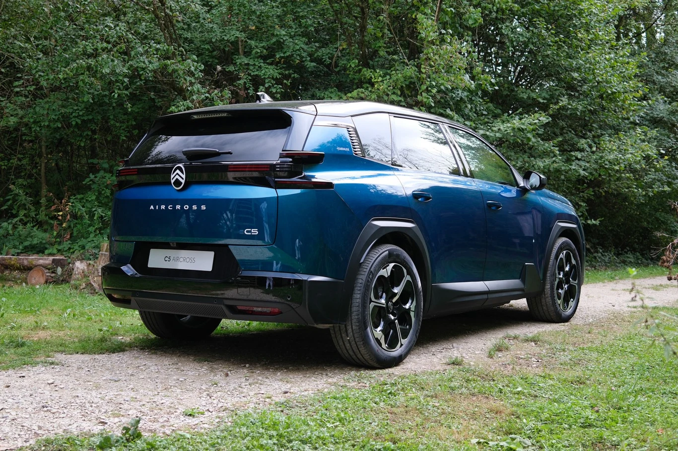 Nowoczesny, niebieski SUV Citroën C5 Aircross zaparkowany na leśnej drodze z widocznymi czarnymi felgami i charakterystycznym, masywnym tyłem auta.