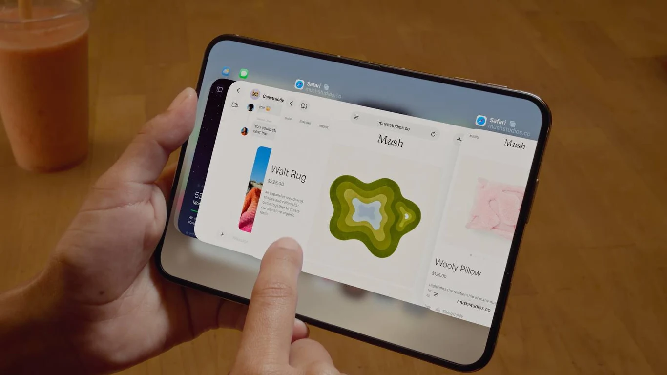 Tablet trzymany w dłoniach wyświetlający aplikację do zakupów online, na ekranie prezentowane są różne produkty i szczegóły jednego z nich, po lewej stronie widoczna szklanka z napojem pomarańczowym.