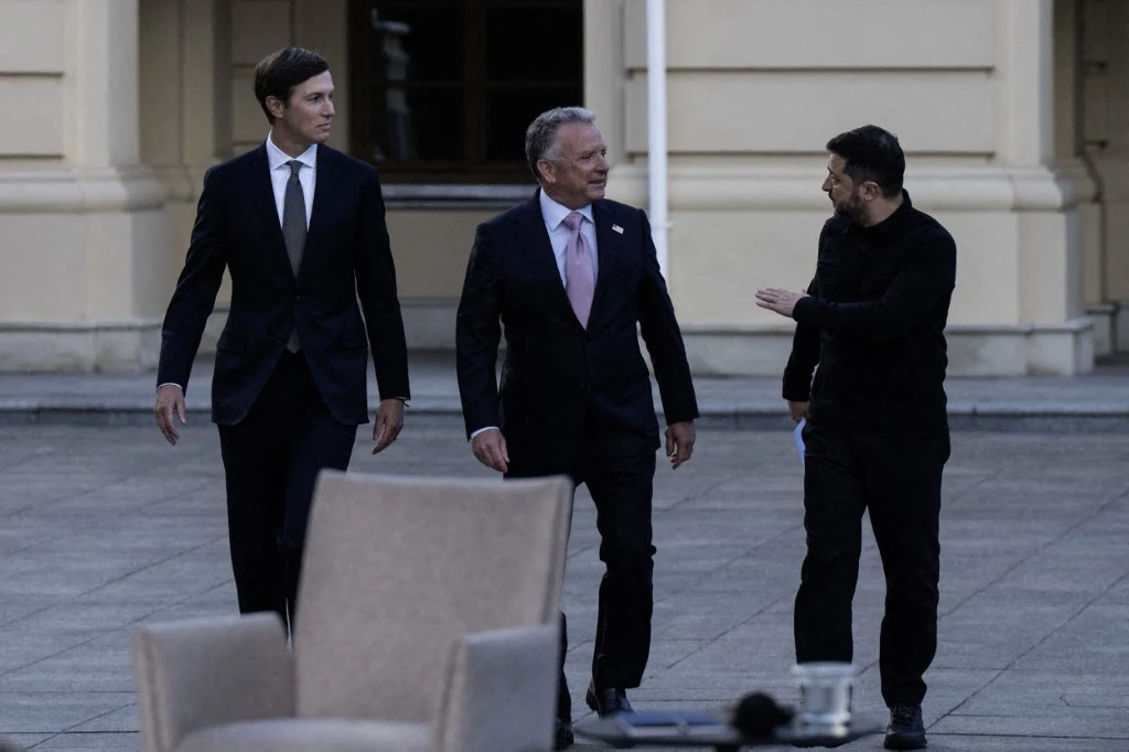 Jared Kushner, Steve Witkoff i Wołodymyr Zełenski Jared Kushner, Steve Witkoff i Wołodymyr Zełenski idą razem po brukowanym placu obok jasnego budynku.