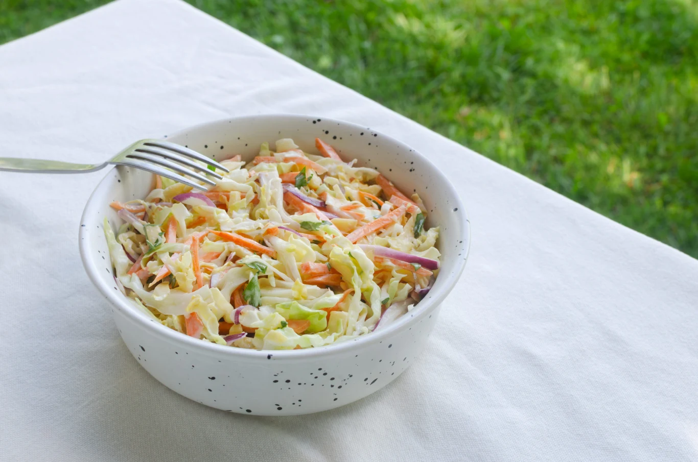 Najlepsza surówka do dań z rybą Miska surówki coleslaw z kapustą, marchewką i czerwoną cebulą oraz widelcem na białym obrusie