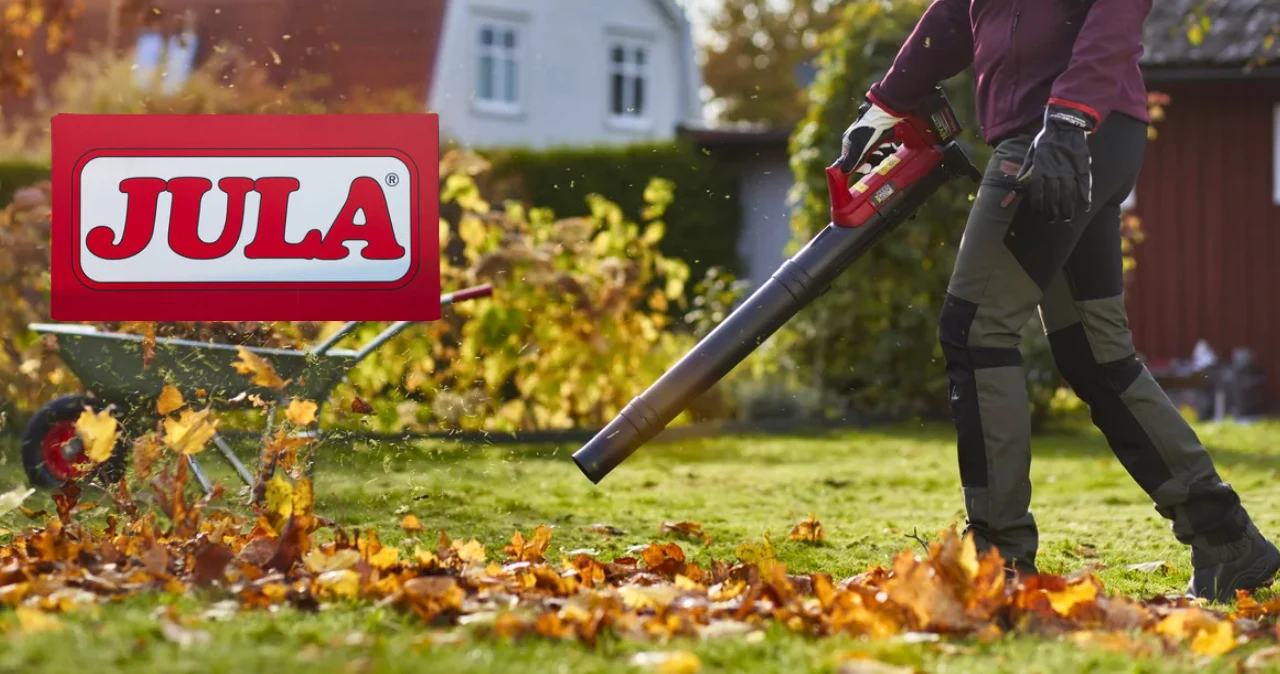 Jula rusza z ofertą Meec Tools. Te 4 sprzęty przydadzą się do jesiennych prac w ogrodzie Osoba w rękawicach używa dmuchawy do liści Meec Tools na trawniku, z taczką pełną liści i logo Jula z lewej.