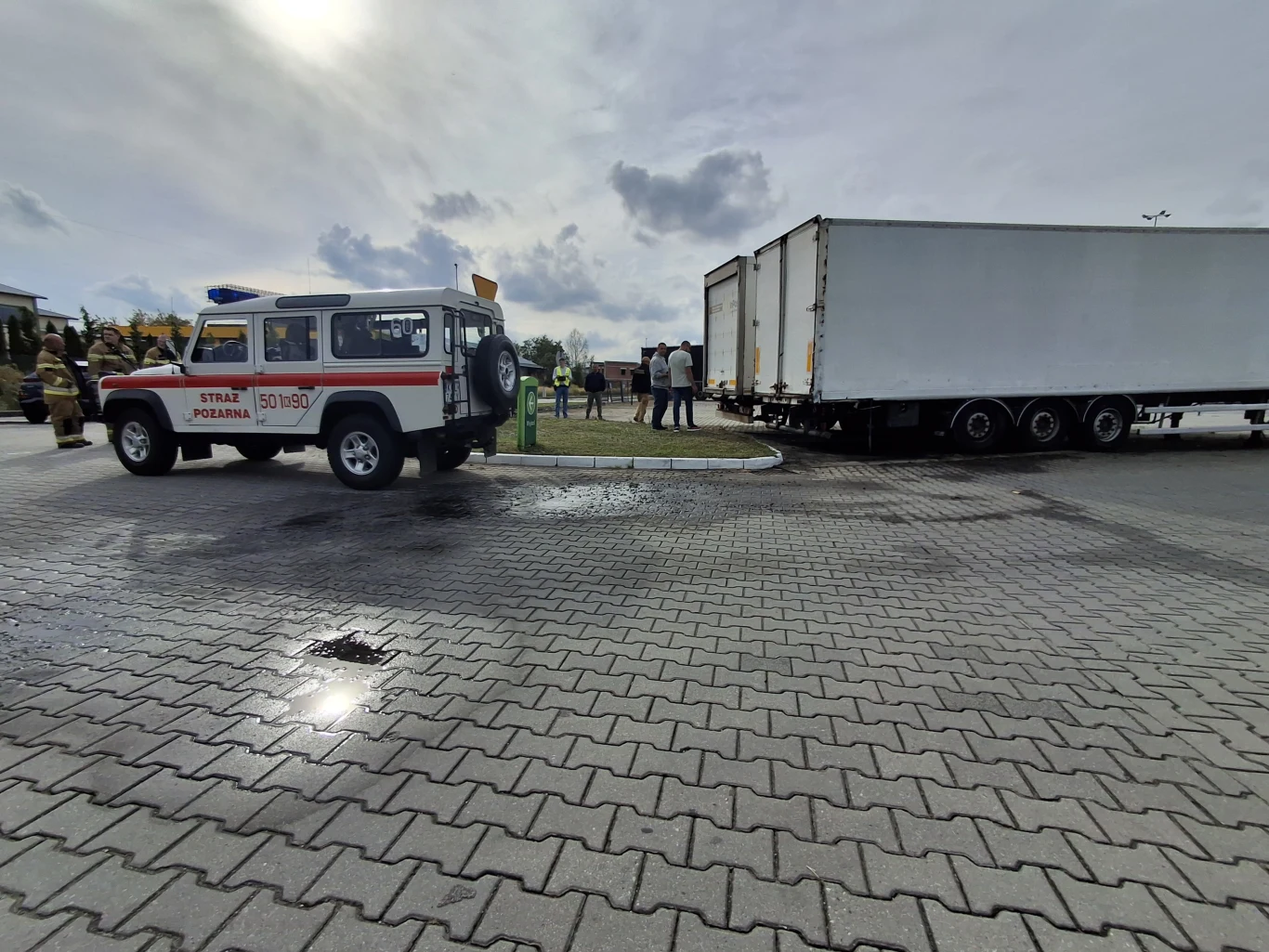 Działania służb na stacji benzynowej w Bolesławiu Samochód straży pożarnej oraz duża naczepa ciężarowa ustawione na parkingu, wokół nich kilku ludzi obserwujących sytuację.