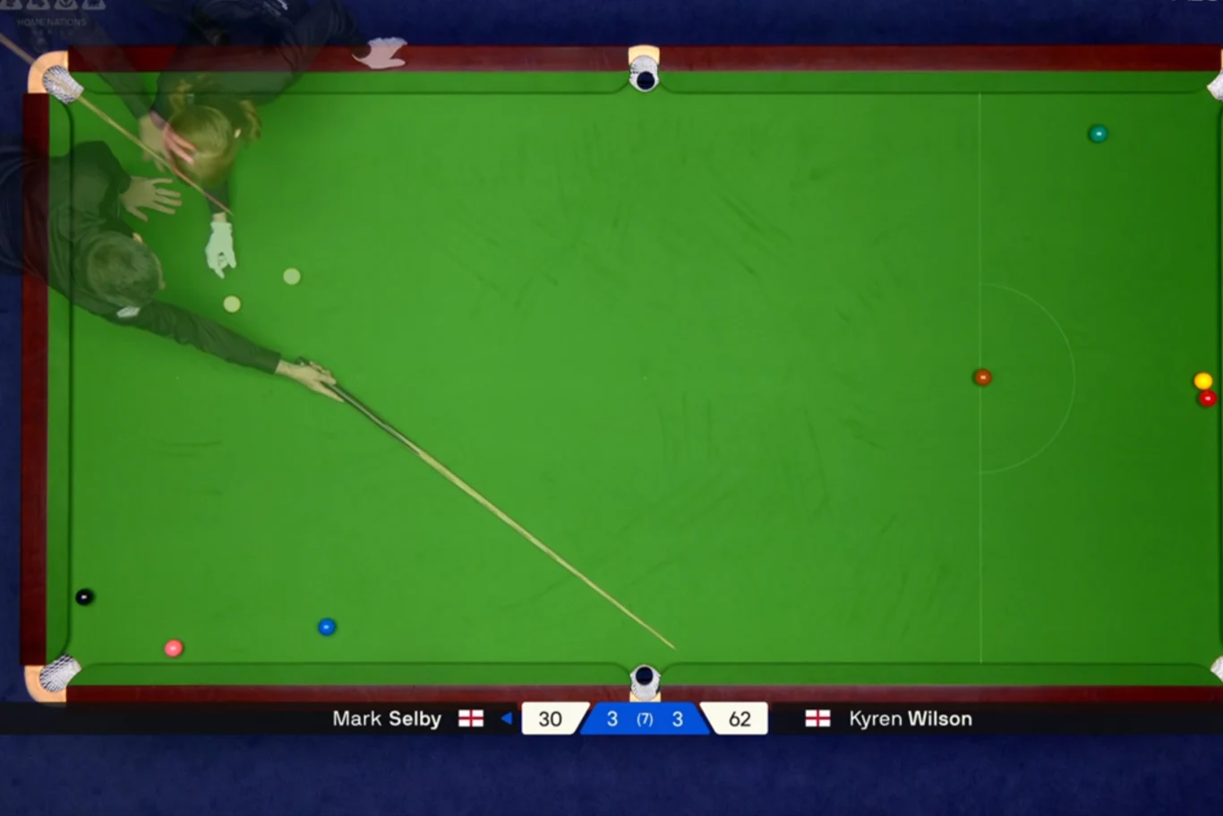 Zawodnik uderzający białą bilę kijem bilardowym na dużym stole snookerowym, wokół rozrzucone kolorowe bile; na dole ekranu widoczne wyniki meczu i nazwiska graczy.