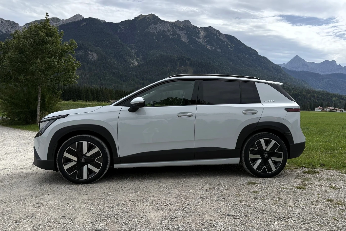 Biały nowoczesny SUV zaparkowany na żwirowej drodze, na tle gór i zielonego pola.