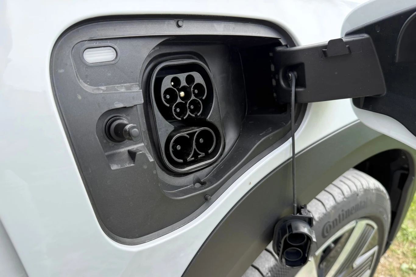 Gniazdo ładowania samochodu elektrycznego z otwartą klapką umieszczone nad tylnym kołem pojazdu.