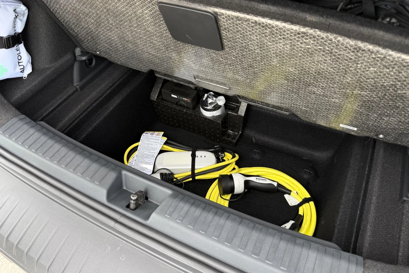 Schowek pod podłogą bagażnika zawierający zwinięty kabel do ładowania samochodu elektrycznego oraz ładowarkę.