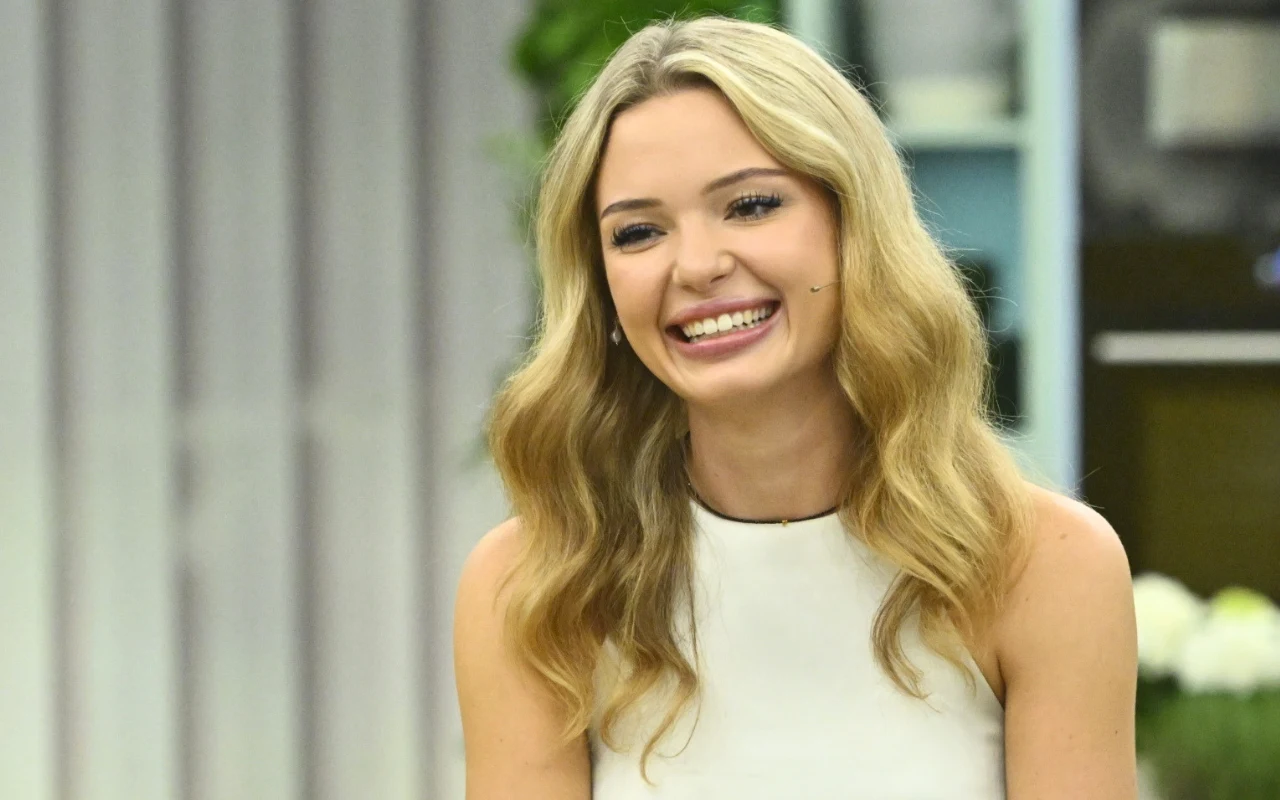 Julia Majchrzak w "halo tu polsat" Uśmiechnięta młoda kobieta o długich, falowanych blond włosach w białej bluzce siedzi we wnętrzu urządzonym w jasnych kolorach.