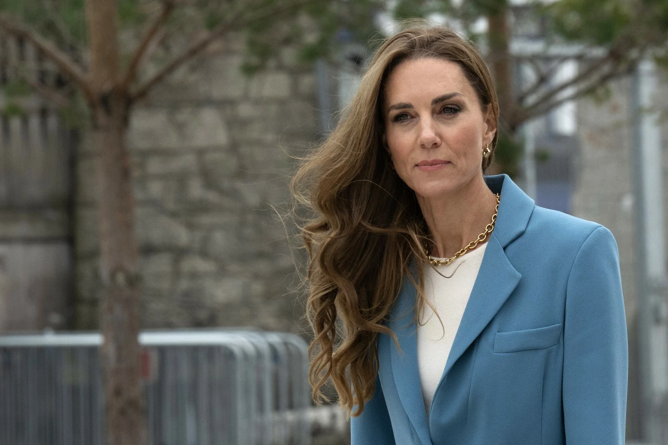 Na ten ważny dzień Kate Middleton wybrała szczególny zestaw biżuterii Kate Middleton w błękitnej marynarce i białej bluzce z naszyjnikiem, stojąca na zewnątrz przy murze i drzewach.