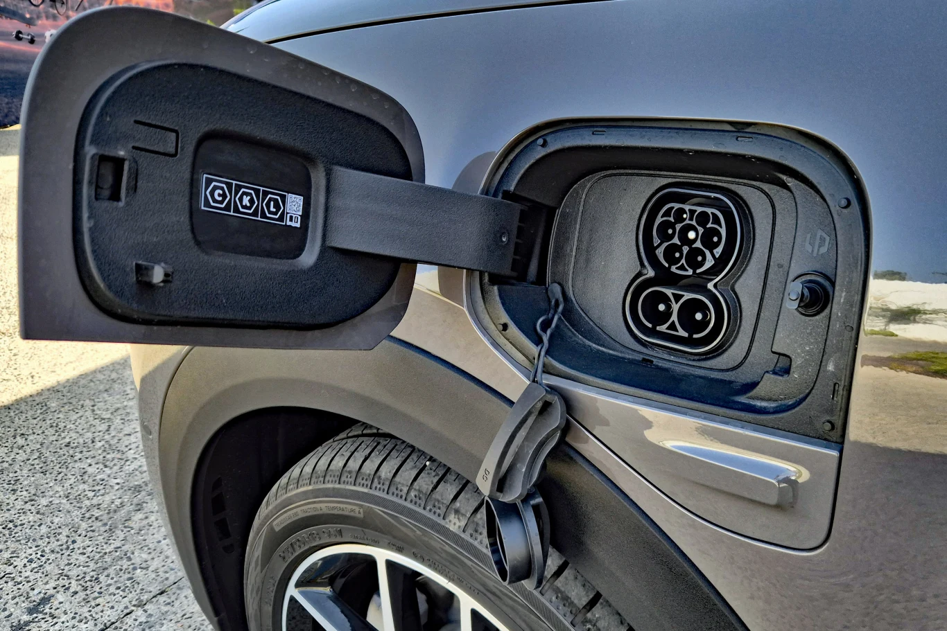 B03X można ładować prądem o mocy 133 kW Gniazdo ładowania samochodu elektrycznego z otwartą klapką, widoczny wzór portu ładowania typu CCS oraz część tylnego nadkola i opony pojazdu.