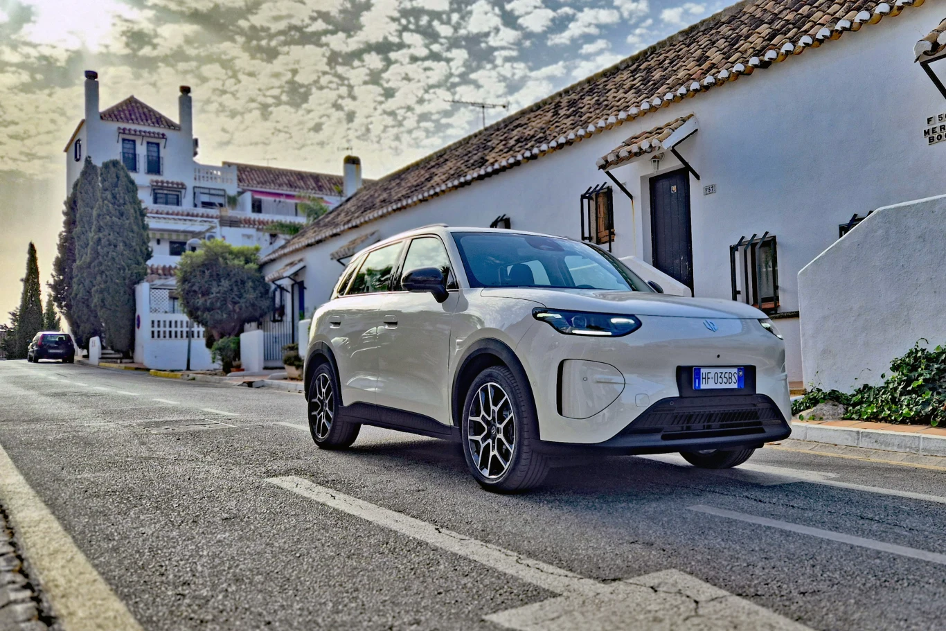 Leapmotor B03X w mocniejszej wersji ma 197 KM, ale jego osiągi bynajmniej nie są sportowe Biały nowoczesny SUV stoi zaparkowany na pustej ulicy przy białych, hiszpańskich budynkach z dachówkami, otoczony subtelną roślinnością i delikatnym światłem dnia.