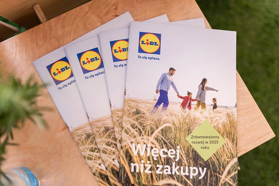 Stosy ulotek Lidl z hasłem „Więcej niż zakupy”, grafiką przedstawiającą rodzinę spacerującą po polu zboża oraz informacją o zrównoważonym rozwoju w 2025 roku.