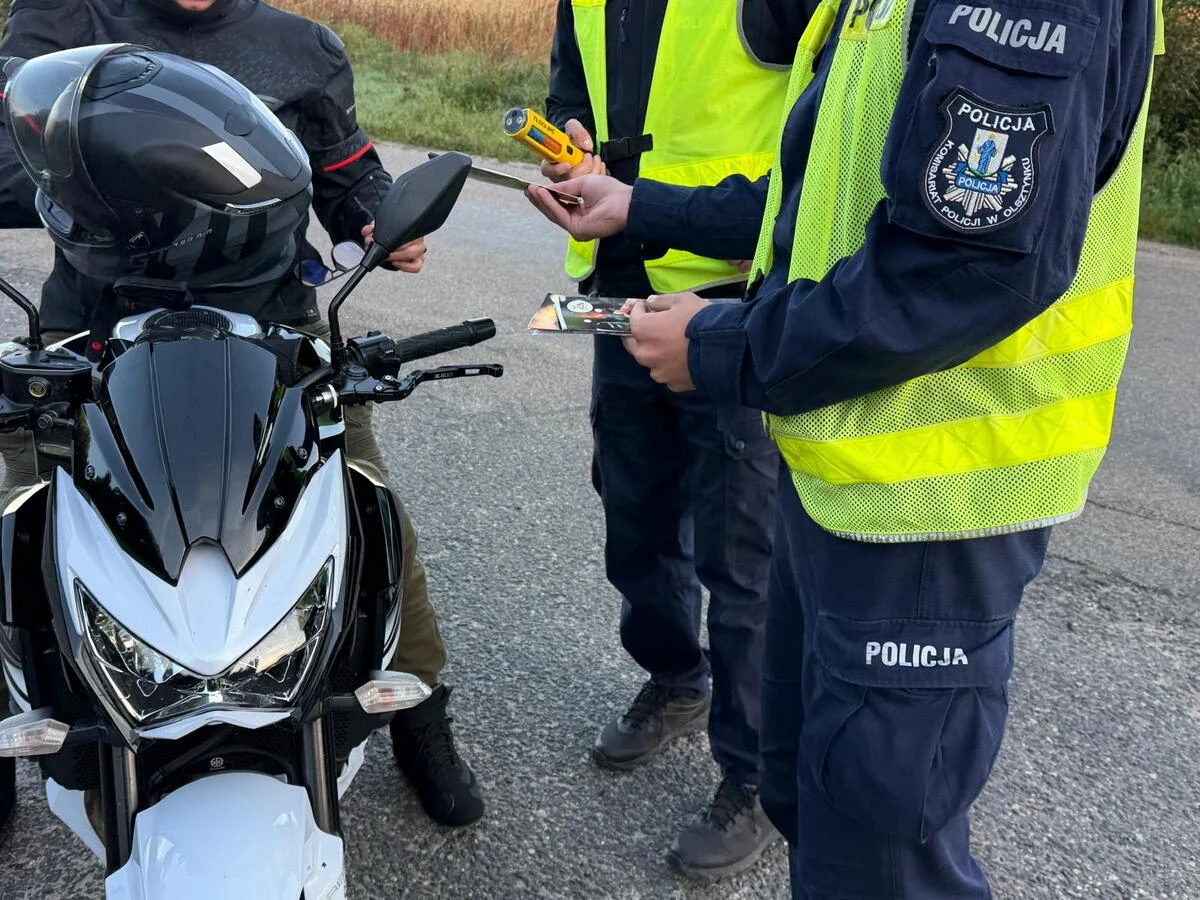 Działania "Trzeźwość" na terenie powiatu olsztyńskiego Policjanci w kamizelkach odblaskowych kontrolują motocyklistę, jeden z nich trzyma alkomat, a drugi dokumenty.