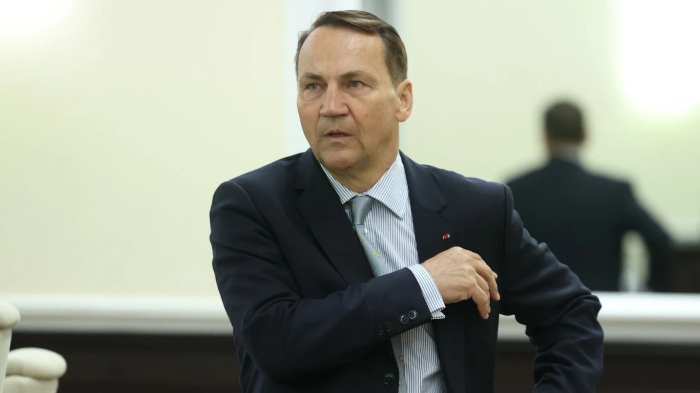 Minister spraw zagranicznych Radosław Sikorski. Zdj. ilustracyjne Radosław Sikorski w garniturze, stoi w jasnym pomieszczeniu, opiera rękę na oparciu fotela.