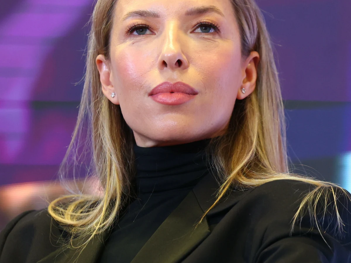 Ewa Chodakowska Ewa Chodakowska w czarnym golfie i marynarce na tle rozmytego fioletowego światła.