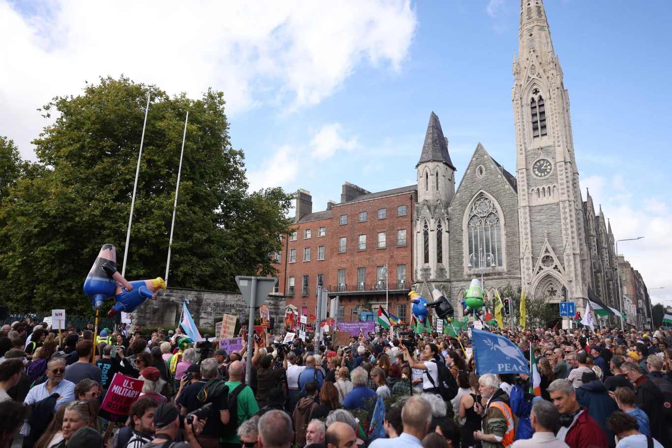 Protesty w Dublinie przeciwko wizycie Donalda Trumpa Tłum protestujących w Dublinie przed zabytkowym kościołem, transparenty i flagi wśród kamienic.