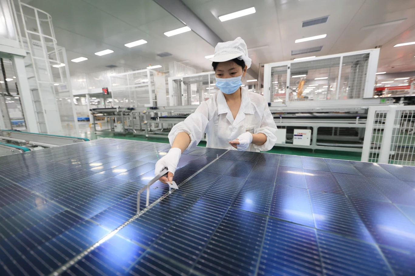 Chiny uzależniły Europę od swoich paneli słonecznych i baterii Pracowniczka w białym kombinezonie i maseczce sprawdzająca duży panel słoneczny w nowoczesnej hali produkcyjnej.