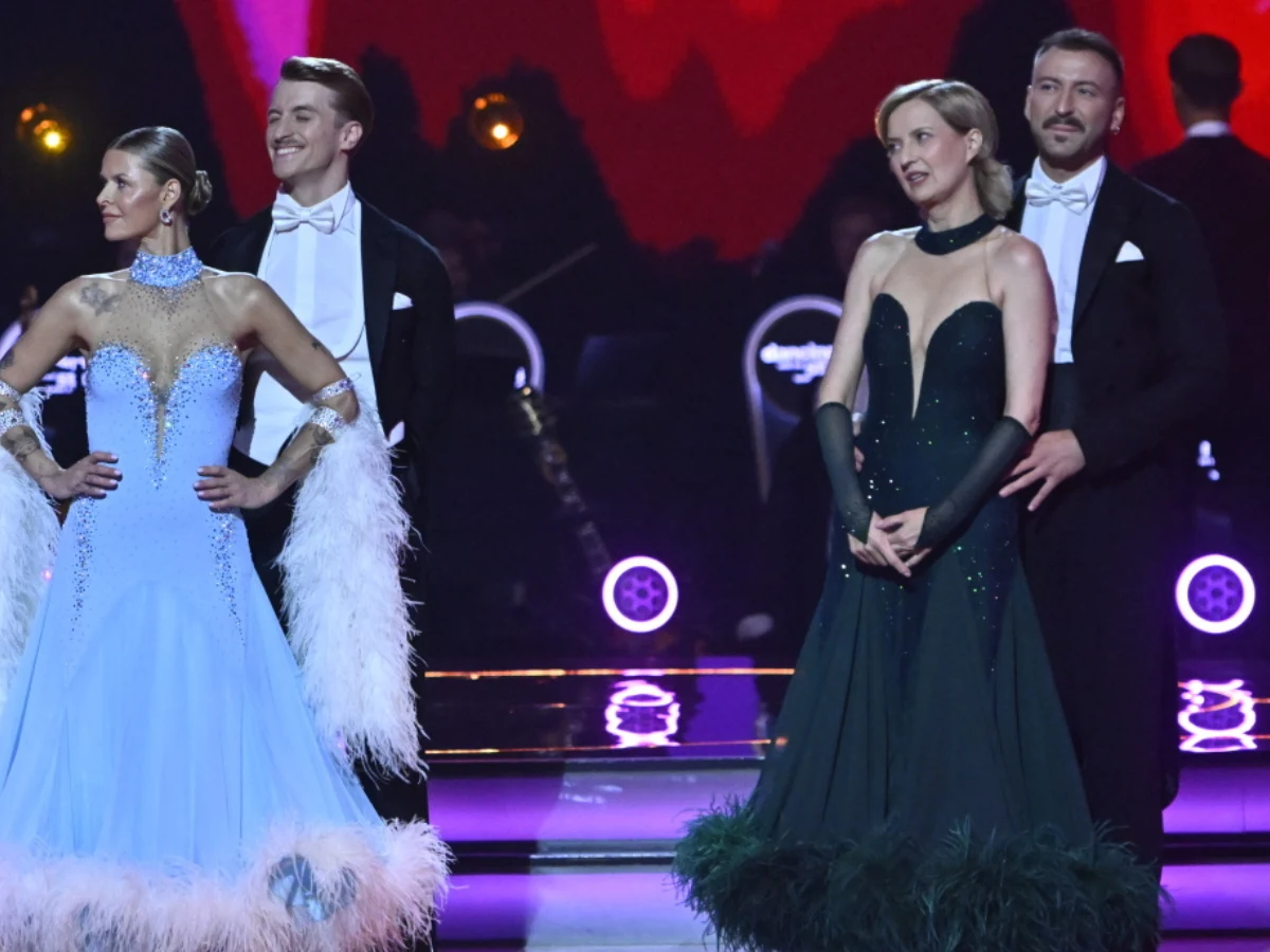 Dwie pary tancerzy w eleganckich strojach wieczorowych stoją na oświetlonej scenie, kobietom towarzyszą długie suknie z piórami, a mężczyźni ubrani są w fraki z białymi muszkami.