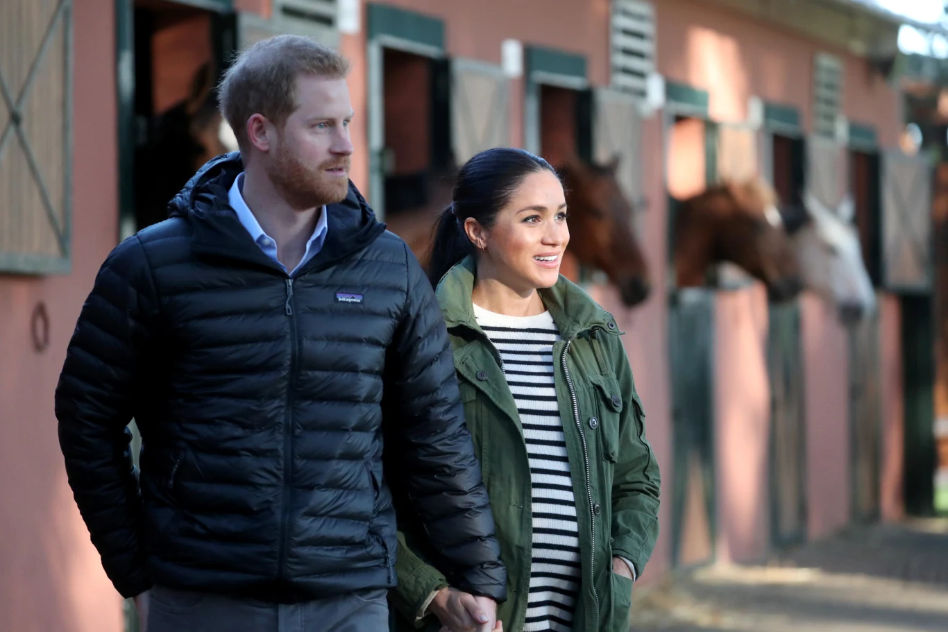 Meghan i Harry mają prowadzić spokojne życie w Wielkiej Brytanii z dala od pełnienia obowiązków związanych z rodziną królewską Para spacerująca obok stajni, w tle widoczne konie wyglądające z boksów.