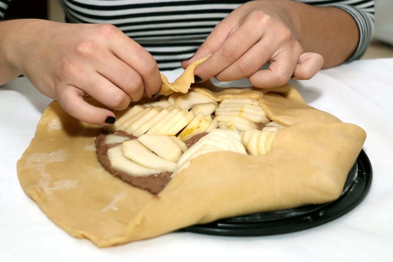 Galette z gruszkami i kremem czekoladowym. Trudno o lepszy deser na jesienne popołudnia Przygotowywanie galette z gruszkami – ręce układają plasterki gruszek na kruche ciasto z kremem czekoladowym.