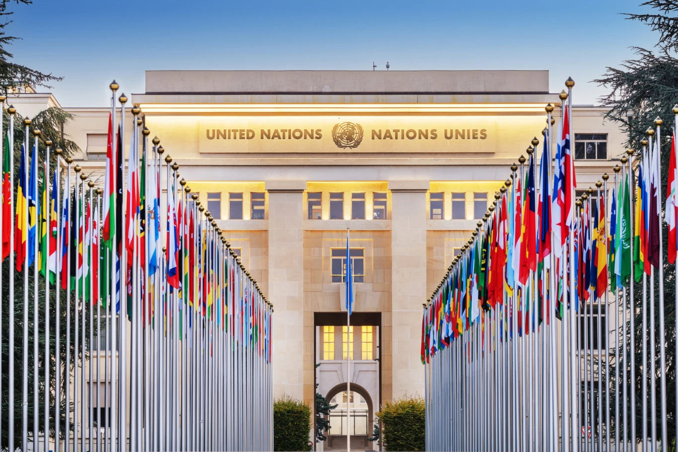 Europejska siedziba ONZ w Genewie Siedziba ONZ w Genewie z napisem United Nations i flagami państw przy wejściu.