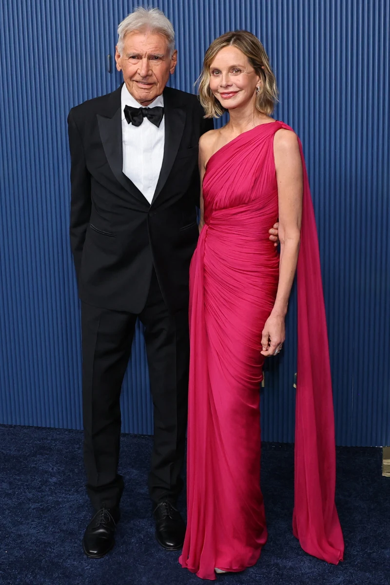 Harrison Ford i Calista Flockhart na gali Emmy Elegancka para w wieczorowych strojach na tle niebieskiej, żłobionej ściany; mężczyzna w czarnym garniturze z muchą, kobieta w długiej, różowej sukni z jednym odkrytym ramieniem.