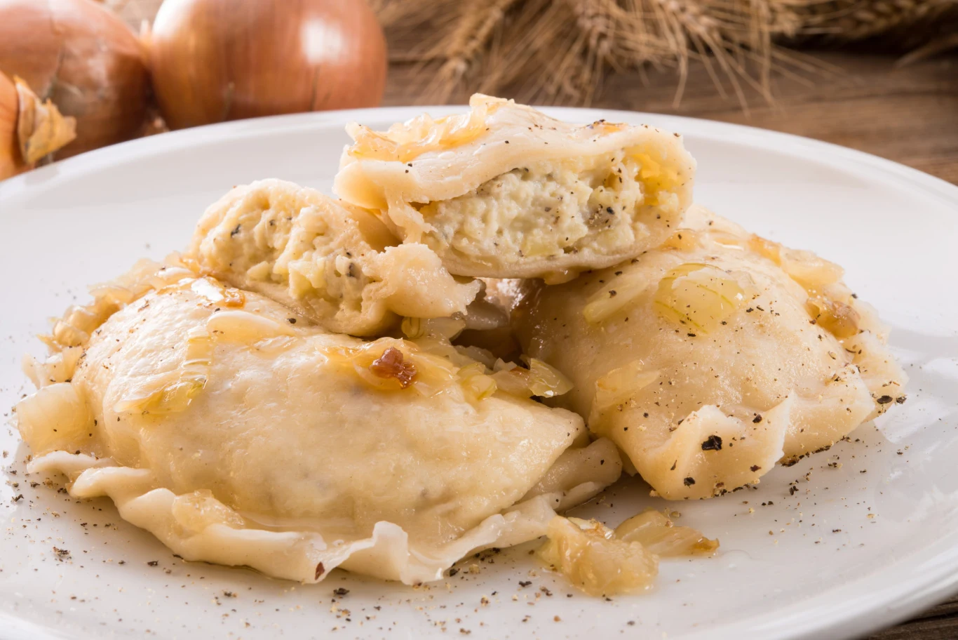 Wystarczy prosta okrasa z cebulki i podstawowe składniki, by zachwycić domowników. Pierogi ruskie z farszem ziemniaczano-serowym, posypane pieprzem i podsmażoną cebulką na talerzu