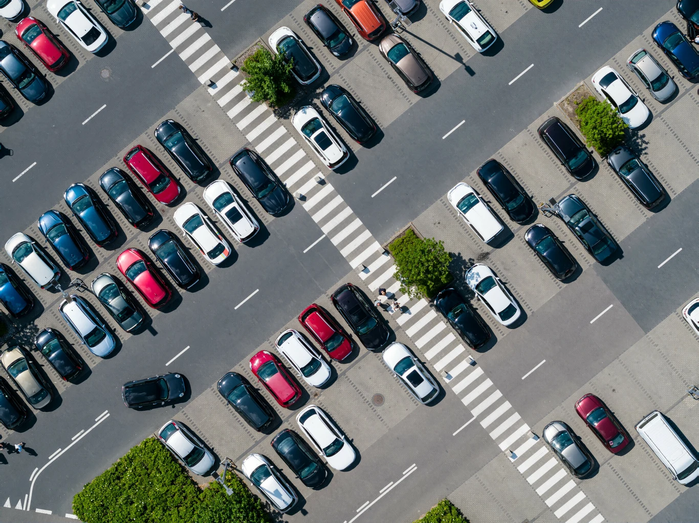 Co w sytuacji, gdy dojdzie do stłuczki "tył w tył" na parkingu? Rzędy zaparkowanych samochodów na dużym parkingu z przejściami dla pieszych i drzewami między miejscami