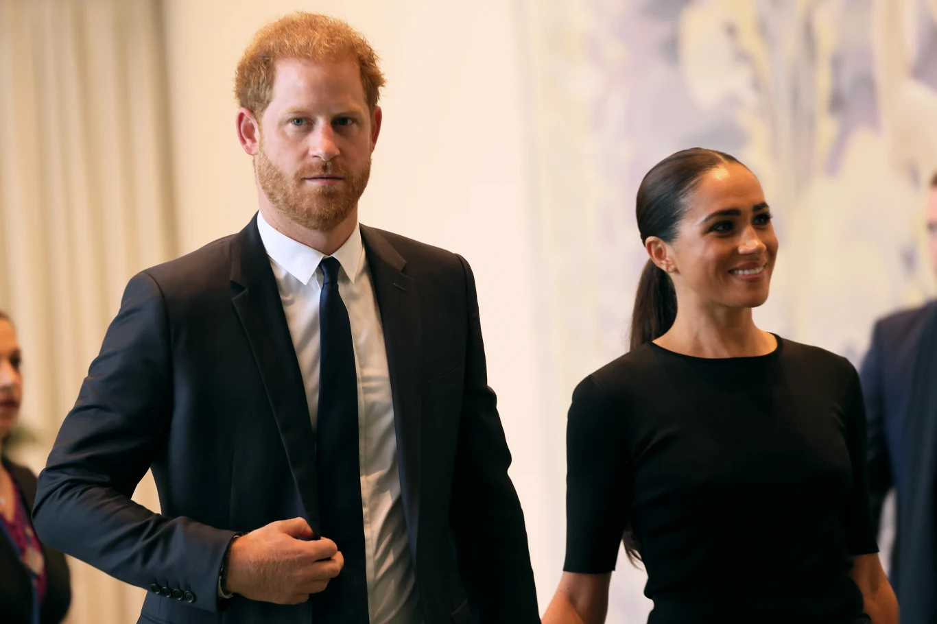 Prywatna szkoła dla dzieci Sussexów miała być niezwykle kosztowna Mężczyzna w garniturze i kobieta w eleganckiej czarnej sukience idą razem, trzymając się za ręce, oboje z poważnym, skupionym wyrazem twarzy.