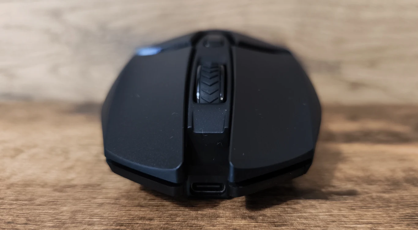 Czarna, nowoczesna mysz komputerowa o wyrazistych krawędziach, widoczna z przodu z rolką przewijania i portem ładowania USB-C, ustawiona na drewnianej powierzchni.