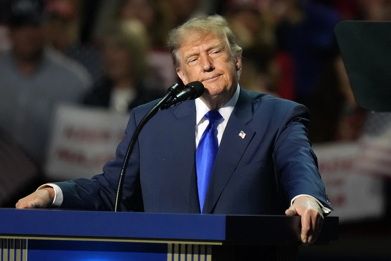 Plany Donalda Trumpa na jesienne wybory do Kongresu znowu się skomplikowały Donald Trump w garniturze i niebieskim krawacie stoi za mównicą z dłońmi na pulpicie; w tle plakaty i ludzie.