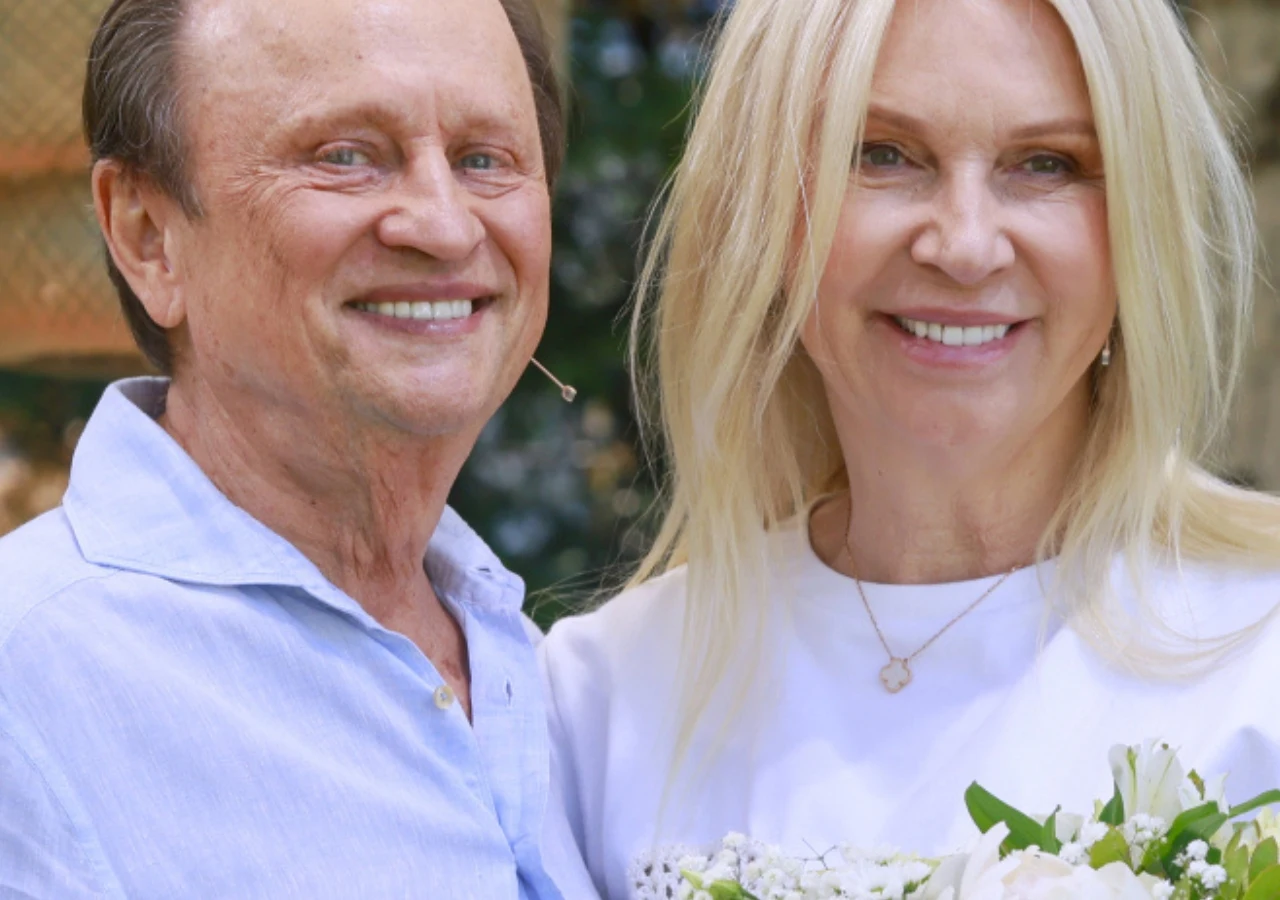 Ryszard Ferenc i Mariola Bojarska-Ferenc Uśmiechnięta para w jasnych ubraniach trzymająca bukiet białych kwiatów.